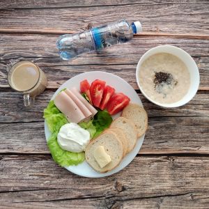 zdjęcie pokazuje Dietę łatwostrawną Kawa zbożowa z mlekiem Owsianka budyniowa z bananem i jabłkiem z posypką chia Bułka pszenna długa krojona Masło extra Serek twarogowy homogenizowany Szynka Drobiowa, parzona, z dodatkiem białka wieprzowego Pomidor Woda mineralna Sałata lodowa